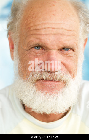 Ein Nahporträt eines älteren Mannes mit weißem Bart und Schnurrbart, hellblauen Augen und grauem Haar. Er trägt ein helles T-Shirt mit weißem Kragen und schaut direkt auf die Stockfoto