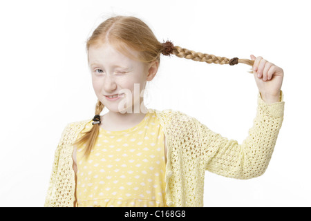 Acht-jährige Mädchen trägt ein gelbes Kleid ziehen ihren Zopf Stockfoto