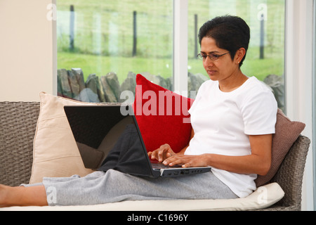 Junge indische asiatische Frau nutzt einen Laptop auf dem sofa Stockfoto