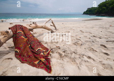 Eine Batik-Sarong drapiert über Login-Treibholz am Strand von Tegal Bias in Padang Bai Bali Indonesien Stockfoto