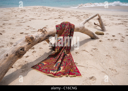 Eine Batik-Sarong drapiert über Login-Treibholz am Strand von Tegal Bias in Padang Bai Bali Indonesien Stockfoto