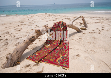 Eine Batik-Sarong drapiert über Login-Treibholz am Strand von Tegal Bias in Padang Bai Bali Indonesien Stockfoto