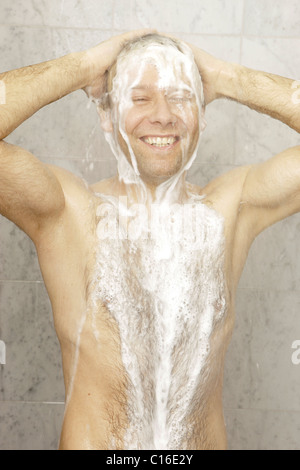 Ein Mann mit Brusthaar ist mit Dusche und eine Menge shampoo Stockfoto