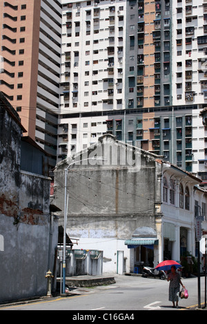 Eine asiatische Frau trägt einen roten Regenschirm während des Gehens unter einem großen Wohnhaus auf einer Stadtstraße in Penang, Malaysia. Stockfoto