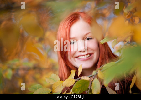 Porträt einer jungen rote kurzhaarige Frau zwischen herbstlichen Blättern in einem Wald Stockfoto