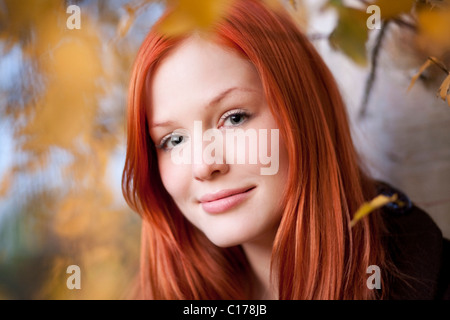 Porträt einer jungen rote kurzhaarige Frau zwischen herbstlichen Blättern in einem Wald Stockfoto