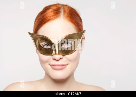 Junge rothaarige Frau trägt eine goldene Maske Stockfoto