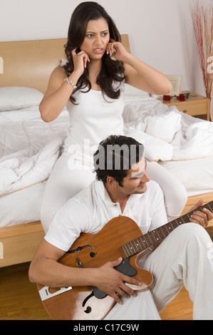 Mann, eine Gitarre zu spielen, mit seiner Frau, indem Finger in Ohren Stockfoto