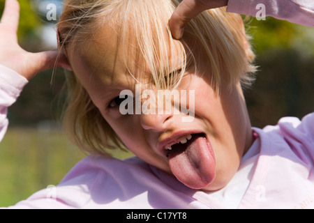 6 Jahre altes Mädchen ihre Zunge heraus und ziehen Gesichter Stockfoto