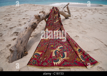 Eine Batik-Sarong drapiert über ein Treibholz-Protokoll auf dem weißen Sand Strand von Bias Tegal in Padang Bai, Bali Stockfoto