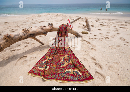 Eine Batik-Sarong drapiert über ein Treibholz-Protokoll auf dem weißen Sand Strand von Bias Tegal in Padang Bai, Bali Stockfoto