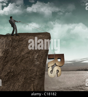 Geschäftsmann, ziehen eine Rupie-Symbol von einer Klippe Stockfoto