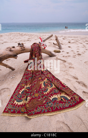 Eine Batik-Sarong drapiert über ein Treibholz-Protokoll auf dem weißen Sand Strand von Bias Tegal in Padang Bai, Bali Stockfoto