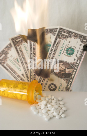 Medizin-Flasche am Tisch mit weißen Tabletten verschütten und vier US-Dollarnoten brennen im Hintergrund Stockfoto