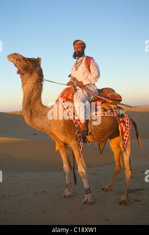 Herr Wüste in traditionellen Rajput, Rajasthani Kleid trägt ein Schwert, ein Kamel reiten auf Sanddünen in der Nähe von Jaisalmer, Rajasthan, Indien Stockfoto