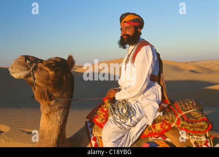 Herr Wüste in traditionellen Rajput, Rajasthani Kleid, sitzt auf einem Kamel auf Sanddünen in der Nähe von Jaisalmer, Rajasthan, Indien Stockfoto