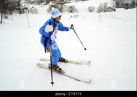 Das junge Mädchen den Berg Skifahrer den Anfänger in blauen Overalls gilt für eine Fahrt auf Abfahrtsski, eine Stadt Domodedowo Stockfoto