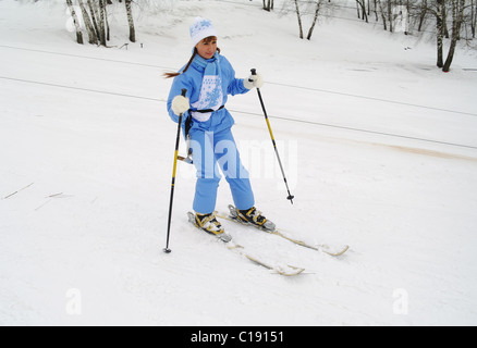 Das junge Mädchen den Berg Skifahrer den Anfänger in blauen Overalls gilt für eine Fahrt auf Abfahrtsski, eine Stadt Domodedowo Stockfoto