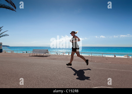 Mädchen-Läufer hört auf ihrem Ipod, wie sie entlang der Promenade des Anglais, Nizza, Alpes-Maritimes, Frankreich verläuft Stockfoto
