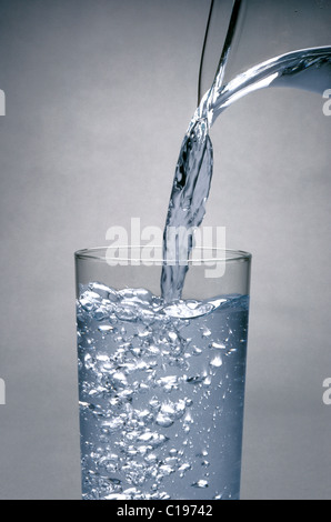 Wasser wird aus Krug in Glas gegossen Stockfoto