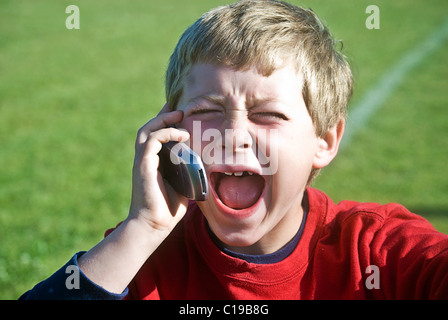 Ein Junge mit weit geöffnetem Mund, er ist entweder lachen oder schreien in das Handy. Stockfoto