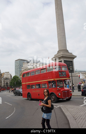 Eine Frau kreuzt die Straße, ein roter Londoner Bus im Laufe der Nelsonsäule in London. Stockfoto