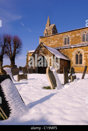Schnee bedeckte Grabsteine vor St. James Church, Burton Lazars, Leicestershire, England, UK Stockfoto