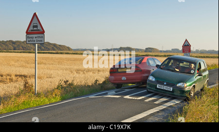 Zwei Autos quetschen vorbei an Geschwindigkeit über bemalte langsam Zeichen auf eine sehr schmale Landstraße Stockfoto