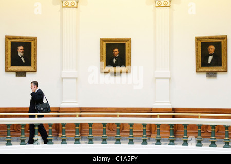 AUSTIN, Texas - ein Mann spricht auf seinem Handy eine der Balkone mit Blick auf das Atrium in der Texas State Capitol Building in Austin, Texas. Hinter ihm sind drei Porträts an der Wand. Stockfoto