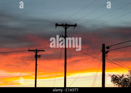 Drei Telefon oder Dienstprogramm oder Strommasten und Linien Silhouette gegen einen hellen, bunten Himmel bei Sonnenuntergang Stockfoto