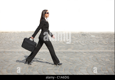 Junge Geschäftsfrau zu Fuß entlang einer gepflasterten Straße vor einer weißen Wand. Stockfoto