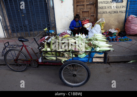 Alte Dame sitzt vor der Tür und Dreiradtaxi barrow voll Mais auf dem Markt, Puno, Peru Stockfoto