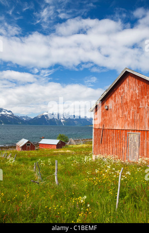 Traditionellen roten Scheunen Linie einen malerischen Fjord, umrahmt von einer schneebedeckten Bergkette, Djupvik, Lyngen Fjord, Troms, Norwegen Stockfoto