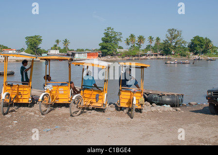 Fahrrad taxis warten auf Kunden und illegal importierte Waren aus Mexiko in Tecun Uman, Guatemala auf den Suchiate-Fluss. Stockfoto