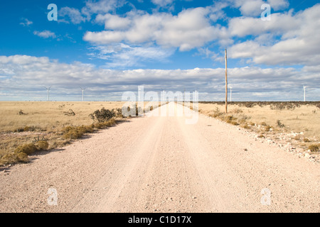 Eine endlose Schotterstraße im nordöstlichen New Mexico führt durch einen riesigen Windpark. Stockfoto