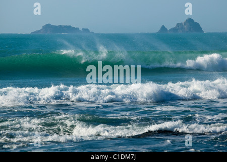 Wellen brechen sich am Strand mit felsigen Inseln im Hintergrund Stockfoto