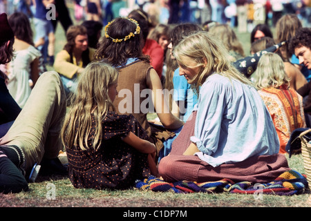 Vintage-Foto von Mutter Frau, die im Gespräch mit Kind Mädchen (ihrer Tochter) in einer Menge Hippies in den 1970er 70er Jahren Mode Kleid sitzend auf einem Feld auf dem Barsham Fair Musikfestival Beccles Suffolk England Großbritannien Großbritannien Großbritannien Großbritannien 1974 KATHY DEWITT Stockfoto