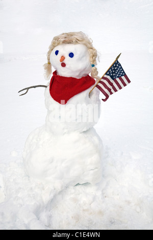 Schnee-Frau trägt einen roten Schal und hält eine amerikanische Flagge. Stockfoto