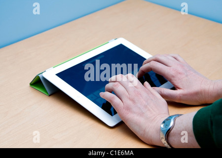 Weibliche Benutzer Hände Tippen auf das neue iPad 2 von Apple Mac, auf einem Schreibtisch aus Holz und blauem Hintergrund. Stockfoto