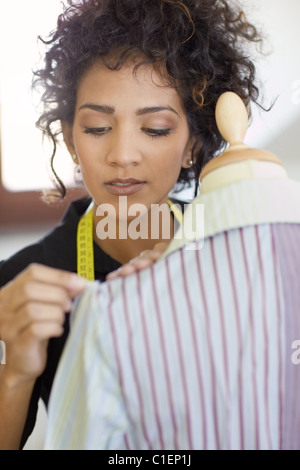 Junge weibliche hispanische Schneiderin anpassen Kleidung auf Schneiderei Mannequin und lächelnd. Vertikale Form, Kopf und Schultern Stockfoto