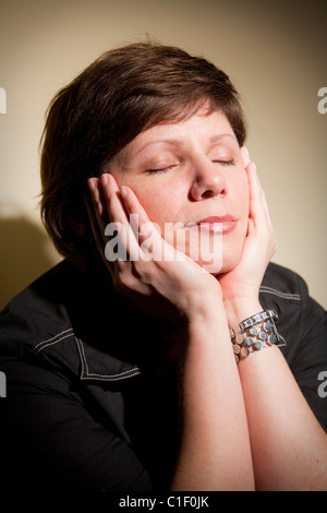 Porträt einer hübschen jungen Frau mit den Händen auf das Gesicht und die Augen geschlossen. Stockfoto
