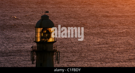 Slangkop Leuchtturm Silhouette gegen die untergehende Sonne reflektiert den Atlantischen Ozean, auf der Cape Peninsula, South Africa Stockfoto
