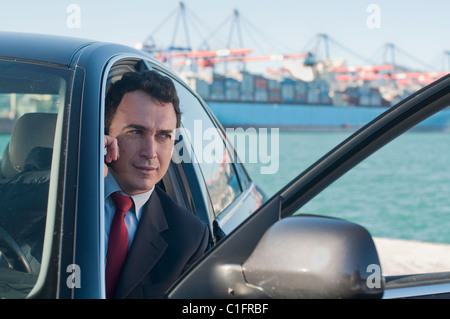 Hispano-Amerikaner Geschäftsmann mit Handy im Auto mit Containerschiff im Hintergrund Stockfoto
