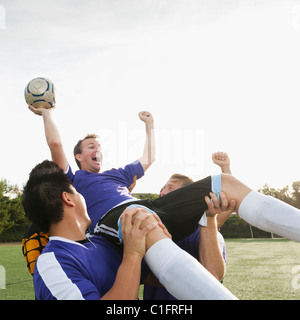 Fußball-Spieler heben Teamkollege und jubeln Stockfoto