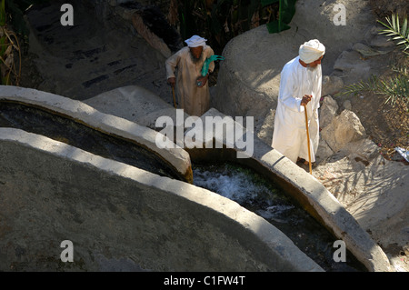 Elder omanischen Männer in traditioneller Kleidung vorbeigehen eine Bewässerung-Kanal, Misfah al-Ibriyeen, Sultanat von Oman Stockfoto