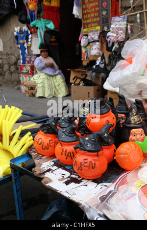 Plastikkürbisse zum Verkauf auf dem Straßenmarkt für Halloween, Aymara Dame sitzt draußen im Geschäft im Hintergrund, La Paz, Bolivien Stockfoto