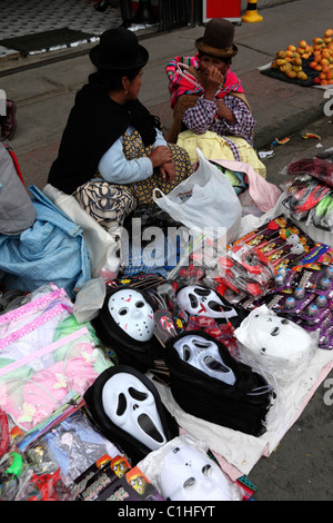 Aymara-Frauen verkaufen weiße Plastik-Geistergesichtsmasken aus den Scream-Filmen auf dem Straßenmarkt für Halloween, La Paz, Bolivien Stockfoto