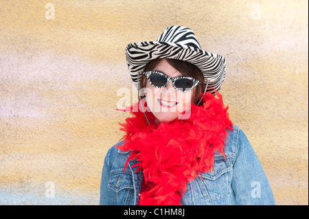 Eine Frau stellt gegen eine gelbe Wand während des Tragens Vintage Tiger gestreift Sonnenbrille und Hut. Stockfoto