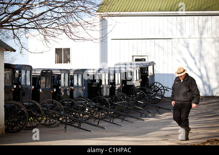 Amische Mann geht vorbei an geparkten Pferd Buggys in einem Stall in Gordonville, PA. Stockfoto