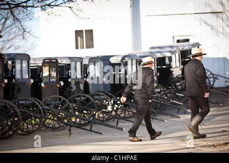 Amische Männer gehen vorbei an geparkten Pferd Buggys in einem Stall in Gordonville, PA. Stockfoto